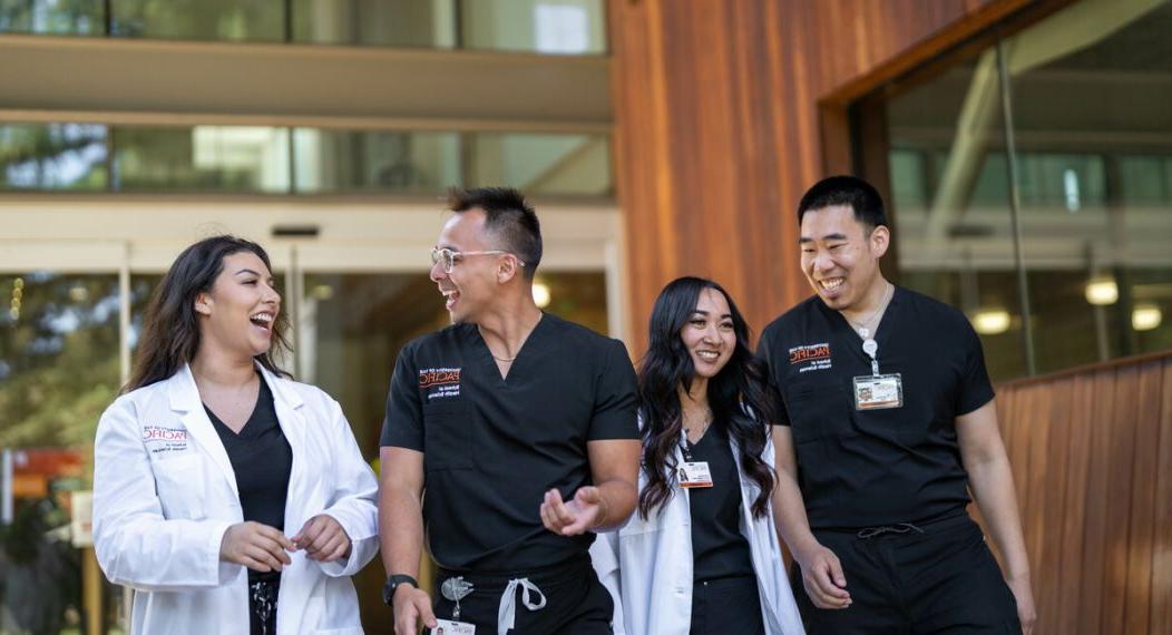 Photo shows four 护理 students at Pacific's 卫生科学学院 talking and smiling while walking out of the nursing classroom.